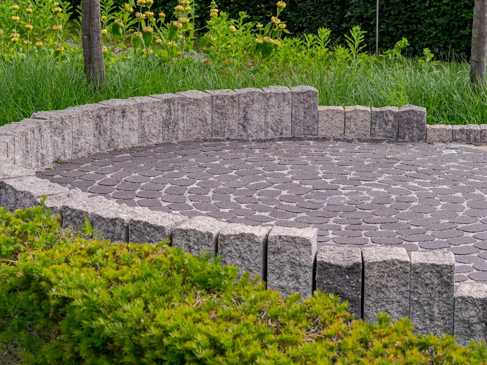 Circular paved patio with a low stone wall and planted borders